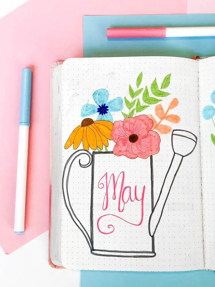 May bullet journal cover page with a watering can and wildflowers