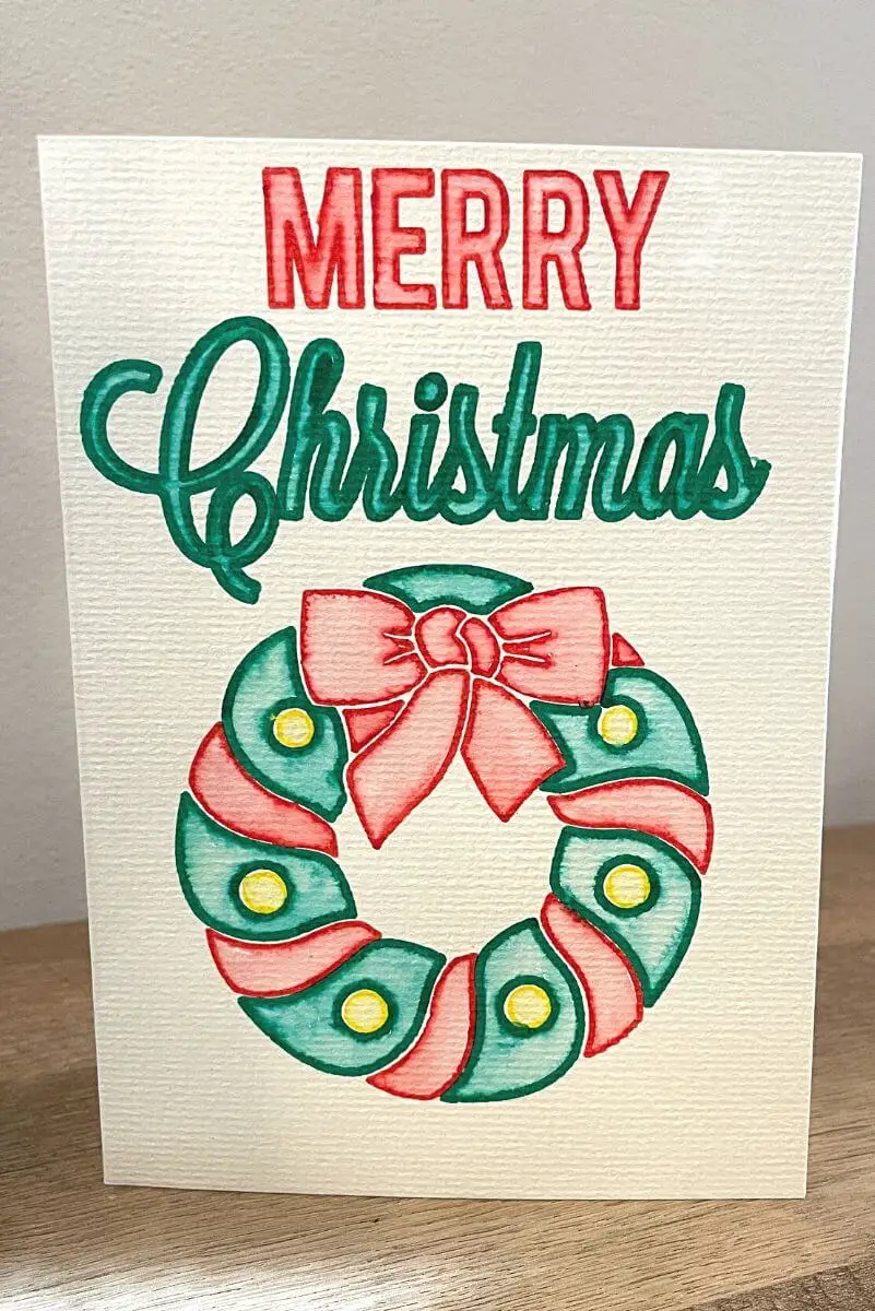Christmas card that reads Merry Christmas with a wreath beneath the text, made with Cricut watercolour markers